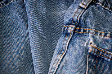 Close up of pair of worn faded blue jeans showing stitching and hole in pocket.