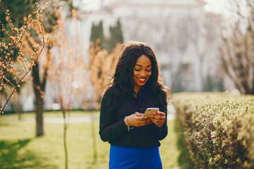 Elegant black woman standing in a summer park. Businesswoman in a blue pants. Lady with phone