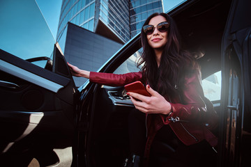 Beautiful smiling women is posing in her new car while chatting on mobile phone. She is wearing red...