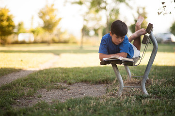Giovane ragazzino sudamericano legge un libro sdraiato su una panchina nel parco sotto casa