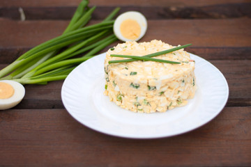 Egg salad with green onions on a white plate against dark wooden background