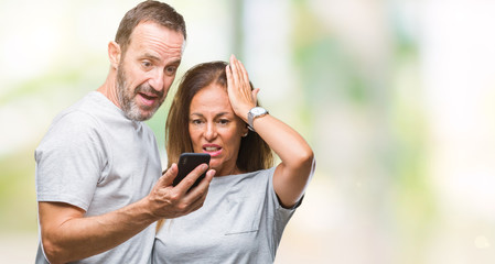Middle age hispanic couple texting message on smartphone ver isolated background stressed with hand on head, shocked with shame and surprise face, angry and frustrated. Fear and upset for mistake.