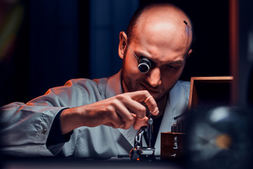 Focused man is working at his workshop with monocle and other tools repairing old watches.