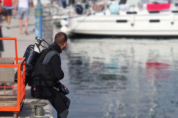 A diver scuba dives in the marina near the pier with sailing yachts. Check for damage below the ship’s waterline after the voyage. Sabbath reception rented boats. Inspectors of the charter company