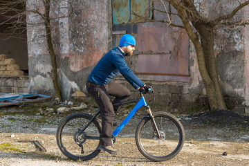 A guy in sportswear riding clothes on a modern mountain carbon bike with an air suspension fork at a vintage brick concrete wall.	