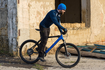 Fototapeta na wymiar A guy in sportswear riding clothes on a modern mountain carbon bike with an air suspension fork at a vintage brick concrete wall. 