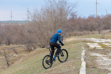 A guy in sportswear riding clothes on a modern mountain carbon bike with an air suspension fork at a vintage brick concrete wall.	