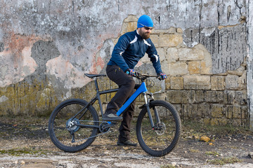 Fototapeta na wymiar A guy in sportswear riding clothes on a modern mountain carbon bike with an air suspension fork at a vintage brick concrete wall. 