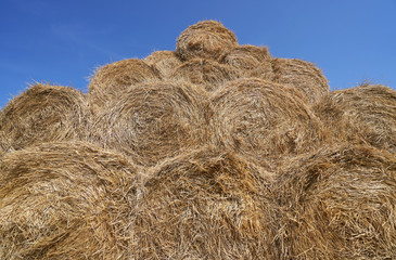 Big haystack from round bales laid in the form of a pyramid against the blue sky