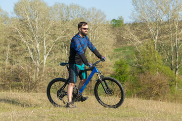 Fototapeta premium Cyclist in shorts and jersey on a modern carbon hardtail bike with an air suspension fork rides off-road on green hills near the forest 