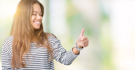 Young beautiful brunette woman wearing stripes sweater over isolated background Looking proud, smiling doing thumbs up gesture to the side