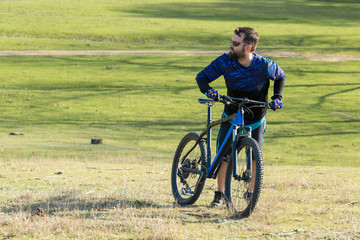 Fototapeta premium Cyclist in shorts and jersey on a modern carbon hardtail bike with an air suspension fork rides off-road on green hills near the forest 