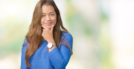 Young beautiful brunette woman wearing blue sweater over isolated background looking confident at the camera with smile with crossed arms and hand raised on chin. Thinking positive.