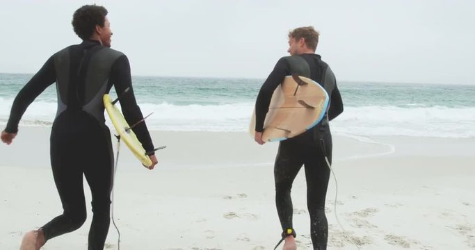 Rear view of two male surfers running together with surfboard on the beach 4k