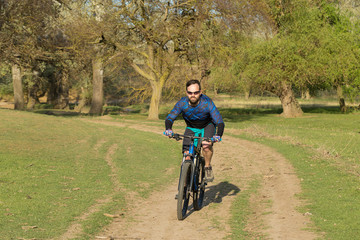 Fototapeta premium Cyclist in shorts and jersey on a modern carbon hardtail bike with an air suspension fork rides off-road on green hills near the forest 