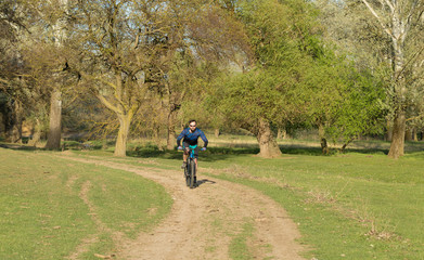 Cyclist in shorts and jersey on a modern carbon hardtail bike with an air suspension fork rides off-road on green hills near the forest	