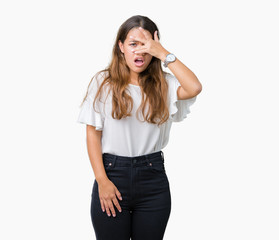 Fototapeta premium Young beautiful brunette business woman over isolated background peeking in shock covering face and eyes with hand, looking through fingers with embarrassed expression.
