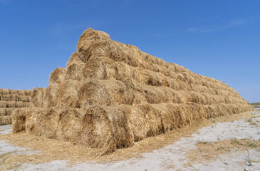 Big haystack from round bales laid in the form of a pyramid against the blue sky