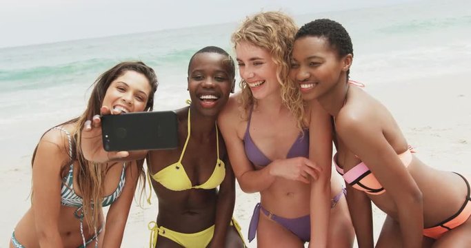 Front view of diverse female friends taking selfie with mobile phone on the beach 4k