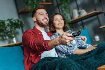 selective focus of happy man holding remote controller while watching movie with woman