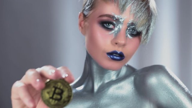 Fashion model woman with trendy metallic make-up showing gold bitcoin coin. Cryptocurrency market concept