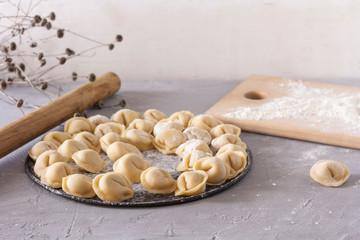 Homemade ravioli on a round platter on the table with flour and rolling pin