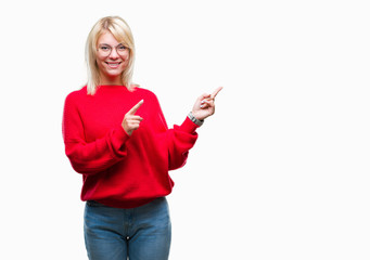 Young beautiful blonde woman wearing sweater and glasses over isolated background smiling and looking at the camera pointing with two hands and fingers to the side.