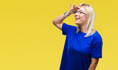 Young beautiful blonde woman wearing glasses over isolated background very happy and smiling looking far away with hand over head. Searching concept.