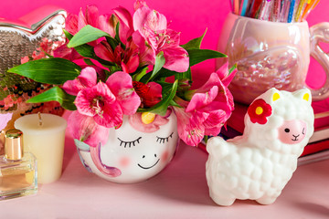 Different Notebooks, alarm clock, unicorn mug, llama squishy, Alstroemeria flowers and flamingo mug with colorful gel pens on bright pink background. Idea of Girly Desk table. Back to school concept