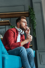 low angle view of handsome man in headphones sitting on sofa and talking on smartphone in living room