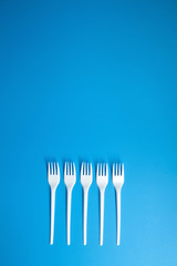 A row of lying white forks on blue background, top view. Disposable plastic tableware