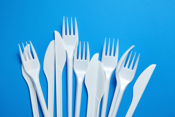 White plastic knives and forks. Disposable plastic tableware on blue background, top view