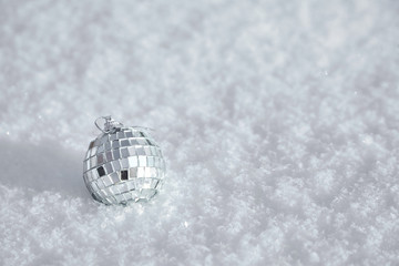 Bauble, toy mirror disco ball lies on the natural snow. Winter Christmas and New Year background. Frosty weather with loose snowy surface in wintertime