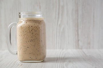 Homemade banana, kiwi, apple smoothie in a glass jar over white wooden background, side view. Copy space.