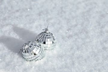 Bauble, toy mirror disco balls lie on the natural snow. Winter Christmas and New Year background. Frosty weather with loose snowy surface in wintertime