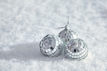 Three toy mirror disco balls lie on the natural snow. Winter Christmas and New Year background. Frosty weather with loose snowy surface in wintertime