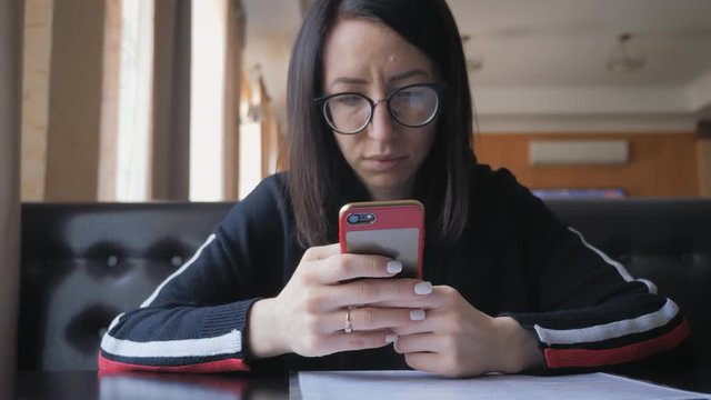 Young wonam use mobile phone while sitting in comfortable coffee shop during work break, charming happy female reading fashion news on cell telephone during breakfast in restaurant.