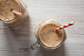 Glass jar filled with banana, kiwi, apple smoothie on a white wooden table, top view. Flat lay, from above, overhead. Close-up.