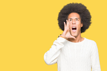 Obraz na płótnie Canvas Young african american man with afro hair wearing winter sweater shouting and screaming loud to side with hand on mouth. Communication concept.