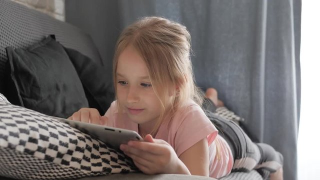 Teenage girl playing on tablet pc resting on a sofa at home. People, technology and leisure concept.