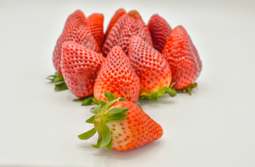 top down view of a group of several tasty fresh red strawberries just harvested and ready to be eaten. The strawberries are put with the green leaves on a white background but one. Horizontal photo
