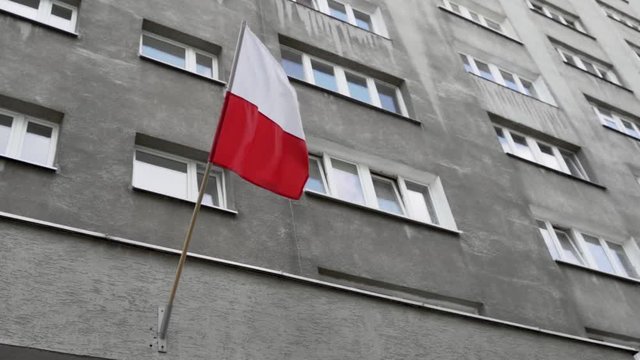 Infinite loop of Polish flag swaying in the wind on Constitution Day (May 3rd) in Warsaw. Flag hangs in front of grey building and is filmed from the ground.