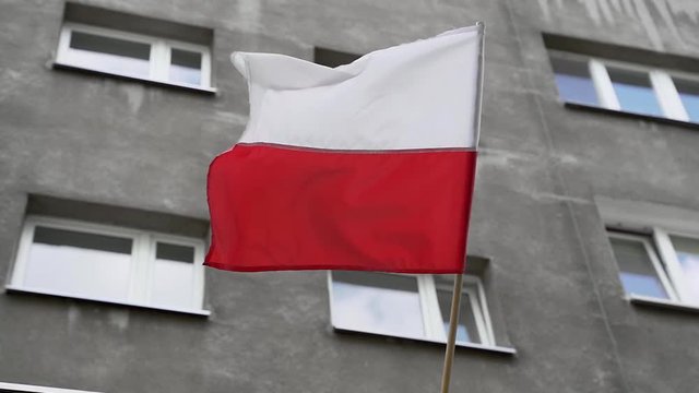 Seamless loop of Polish flag swaying in the wind in front of grey building in Warsaw. Close view, filmed from below.