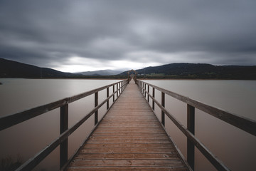 Fototapeta na wymiar Wooden bridge across lake on cloudy day long exposure