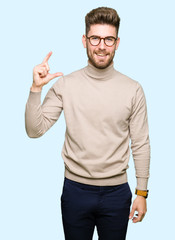 Young handsome business man wearing glasses smiling and confident gesturing with hand doing size sign with fingers while looking and the camera. Measure concept.