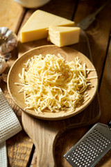 Shredded yellow cheese on wooden plate with cheese grater on kitchen table