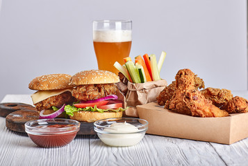deep-fried chicken in a crafting container with two hamburgers, french fries, beer glass, vegetable sticks, sauces