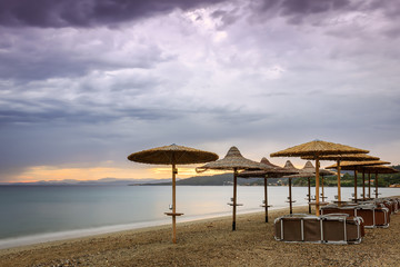 Straw beach parasol, beach beds, purple sunset sky and silky, sea water