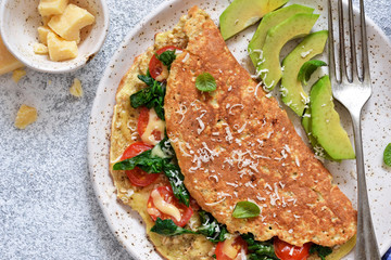 Omelet with tomatoes, cheese and basil in a plate on the kitchen table. View from above.