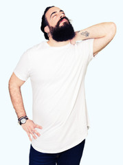 Young hipster man with long hair and beard wearing casual white t-shirt Suffering of neck ache injury, touching neck with hand, muscular pain